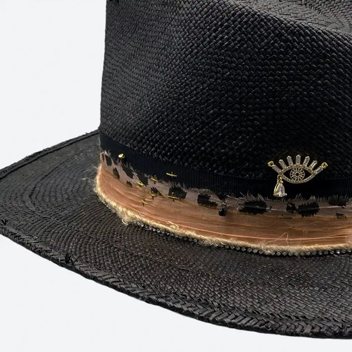 Detail view of a Valeria Andino Handmade Straw Hat, its Classic cowboy shape in black with hand dyed silk trimmings, stones and gold jewelry